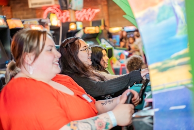 three people playing a racing game at the arcade