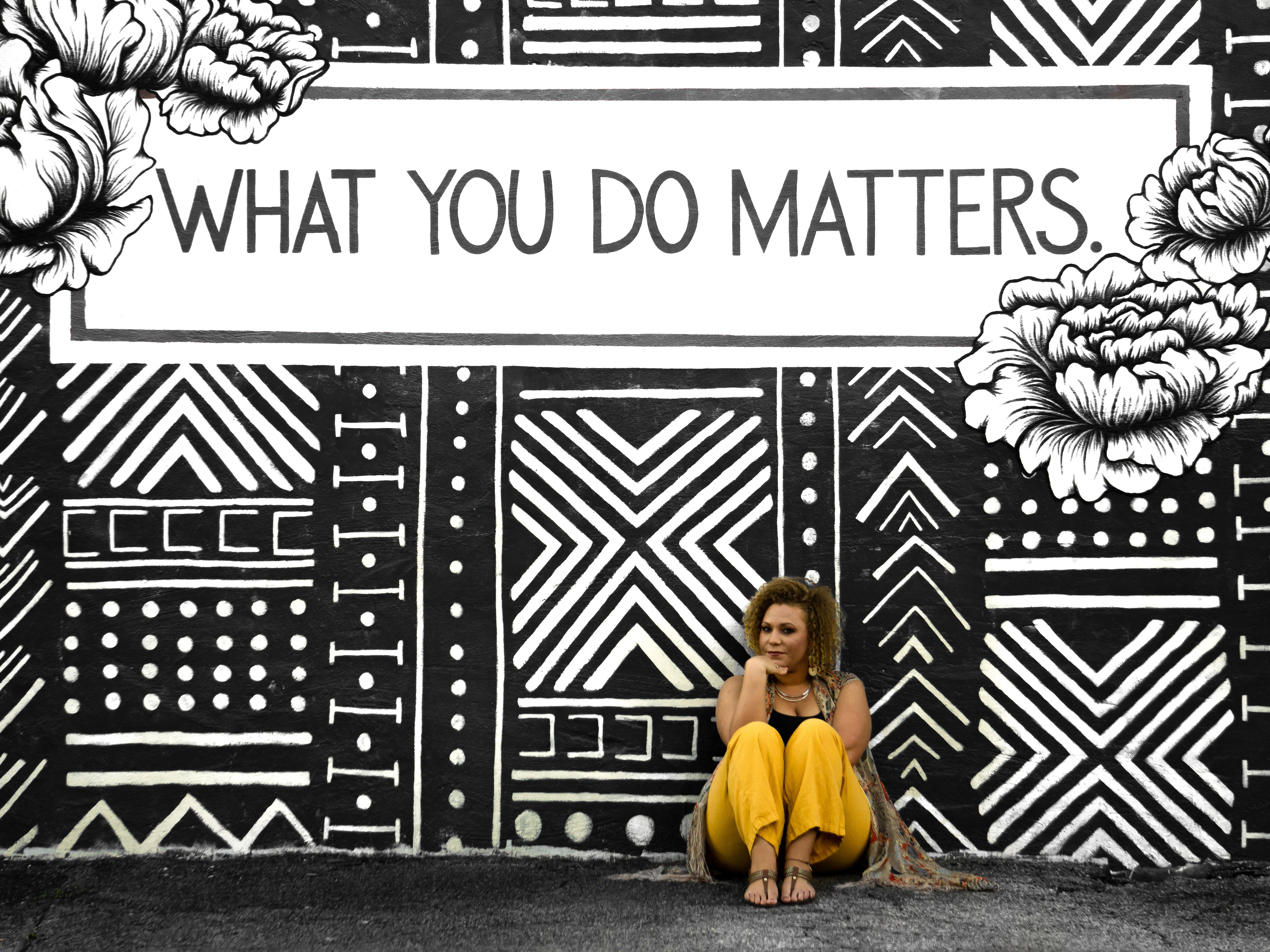 woman sitting by mural that says what you do matters