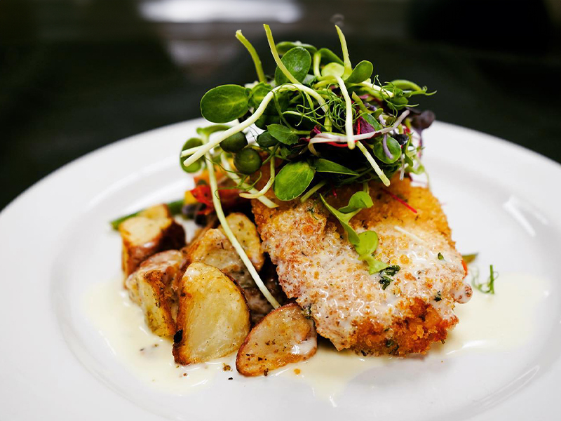 Herb crusted chicken breast with potatos under a bed of greens.