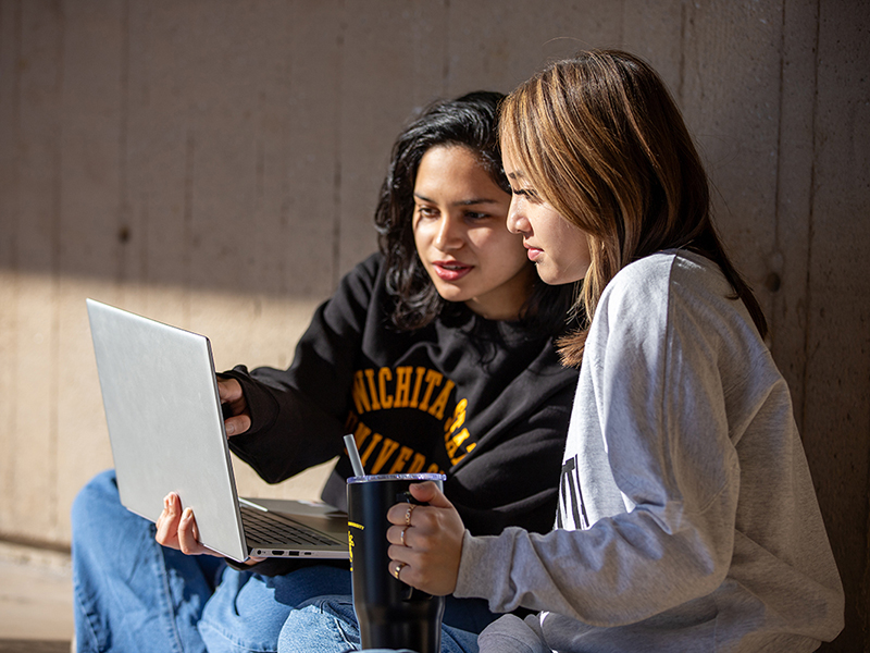 Two students sit on the floor and look at a laptop in McKnight Art Center