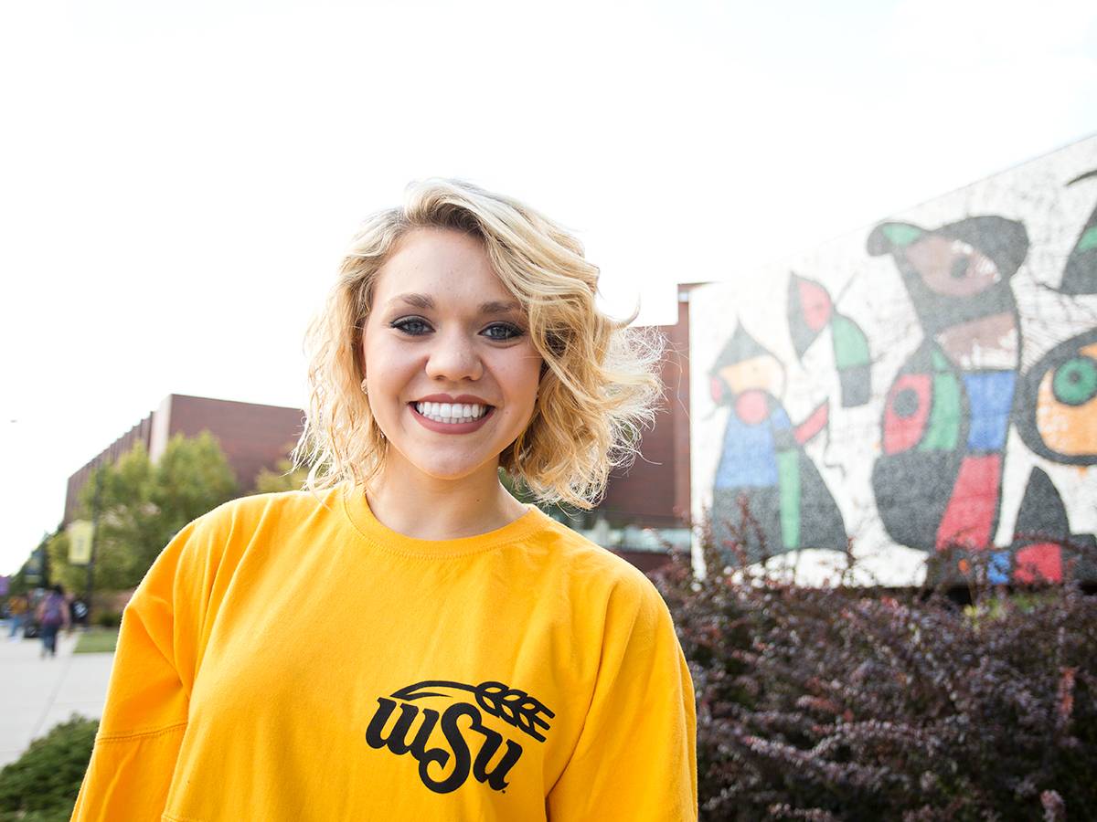 Female student smiling with Joan Miro mural in the background.