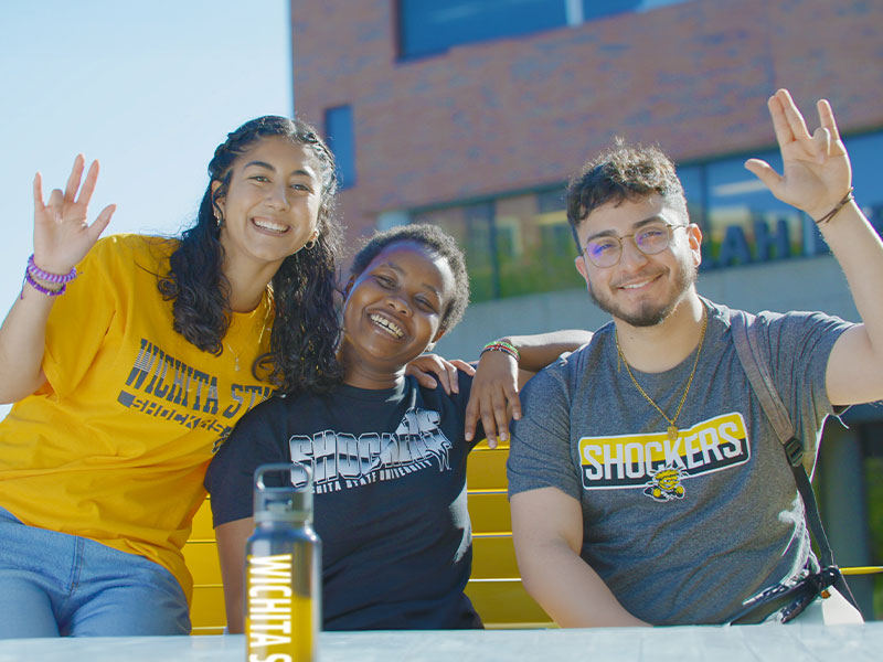 Students smiling together while waving the Shocker hand sign.