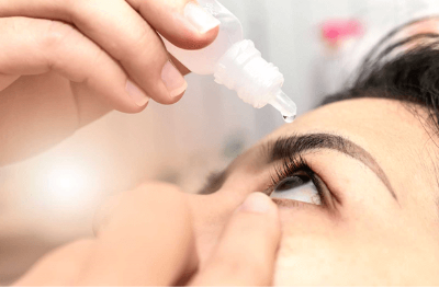 Woman holding eye dropper abover her eye about to put drops in