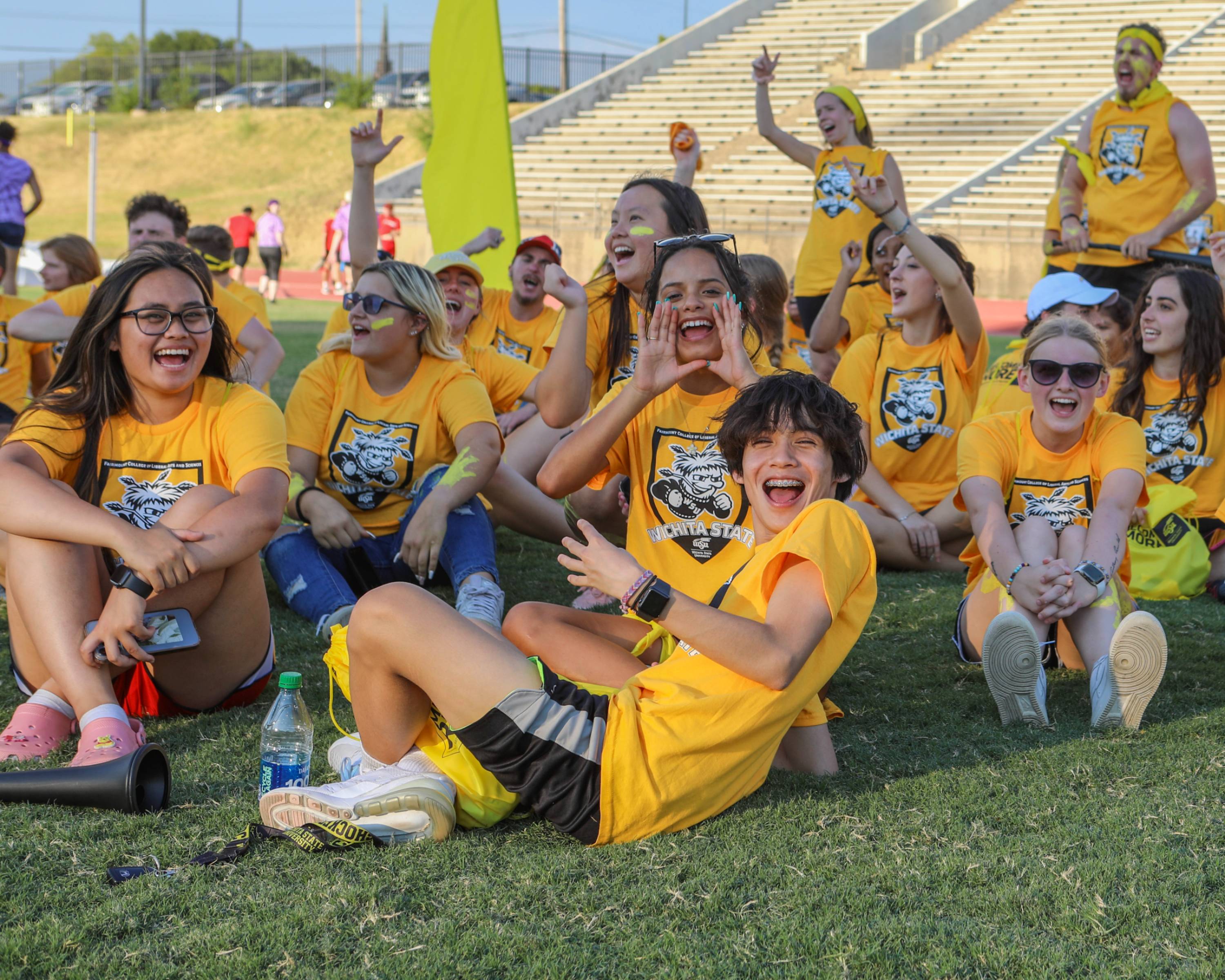 Students sitting outside in yellow shirts cheering for Fairmount College!