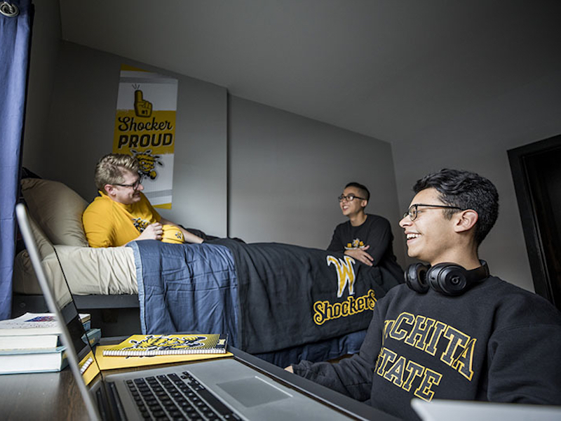 Photo of three students laughing and lounging while working on a project together in an apartment. 