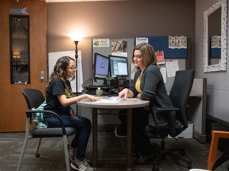An advisor and a student set on opposite sides of a desk reviewing a planning document. 