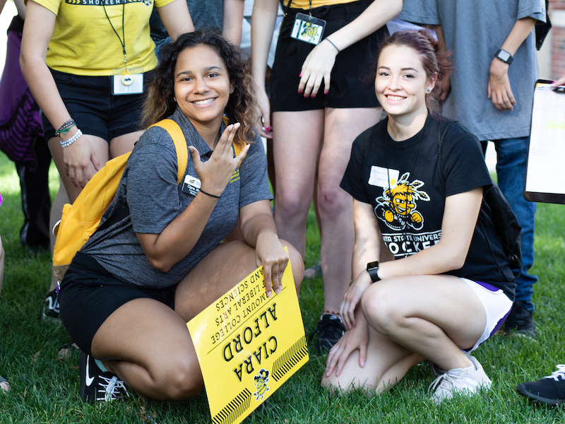 Smiling students make the Shockers hand sign during Orientation gathering. 
