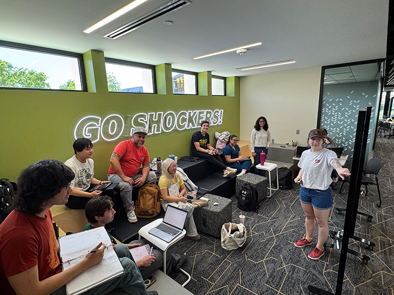 A tutor leads a session for students seated in front of a Shocker neon sign.