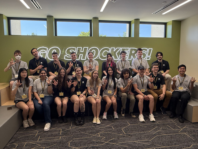 SI leaders gathered for a group photo in front of a Go Shockers neon sign.