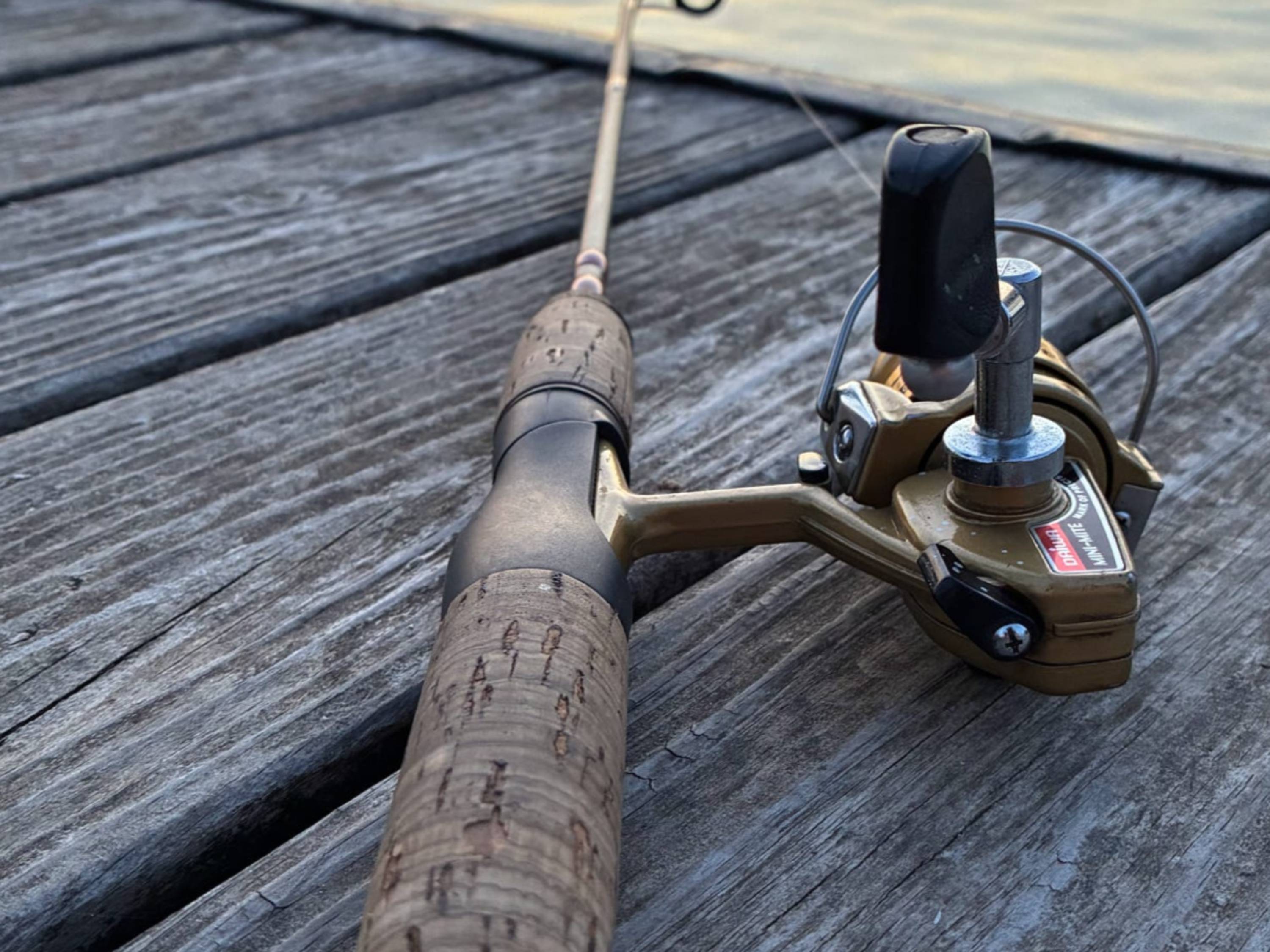 A close-up image of a fishing pole, found laying on top of a wooden dock, looking down toward the tip.