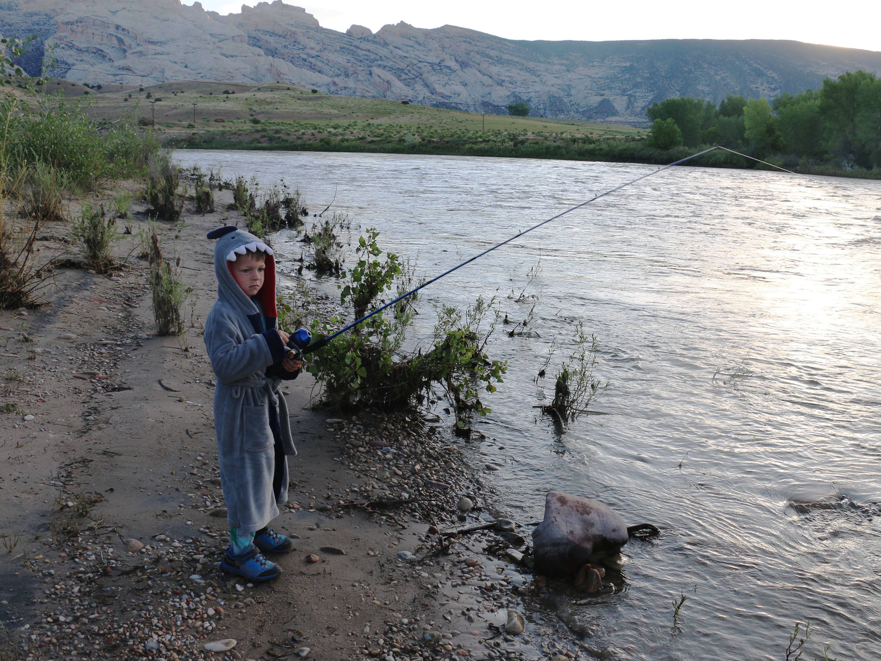 A young boy in a shark robe fishes on a river side