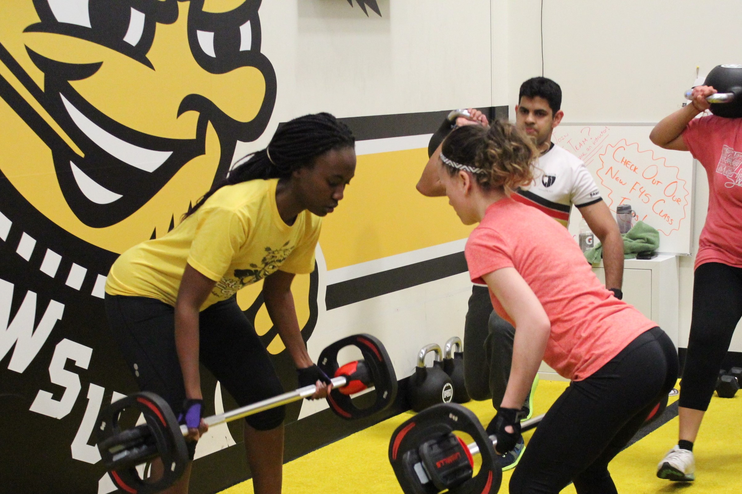 Two women facing each other as they lift weights in the F45 room