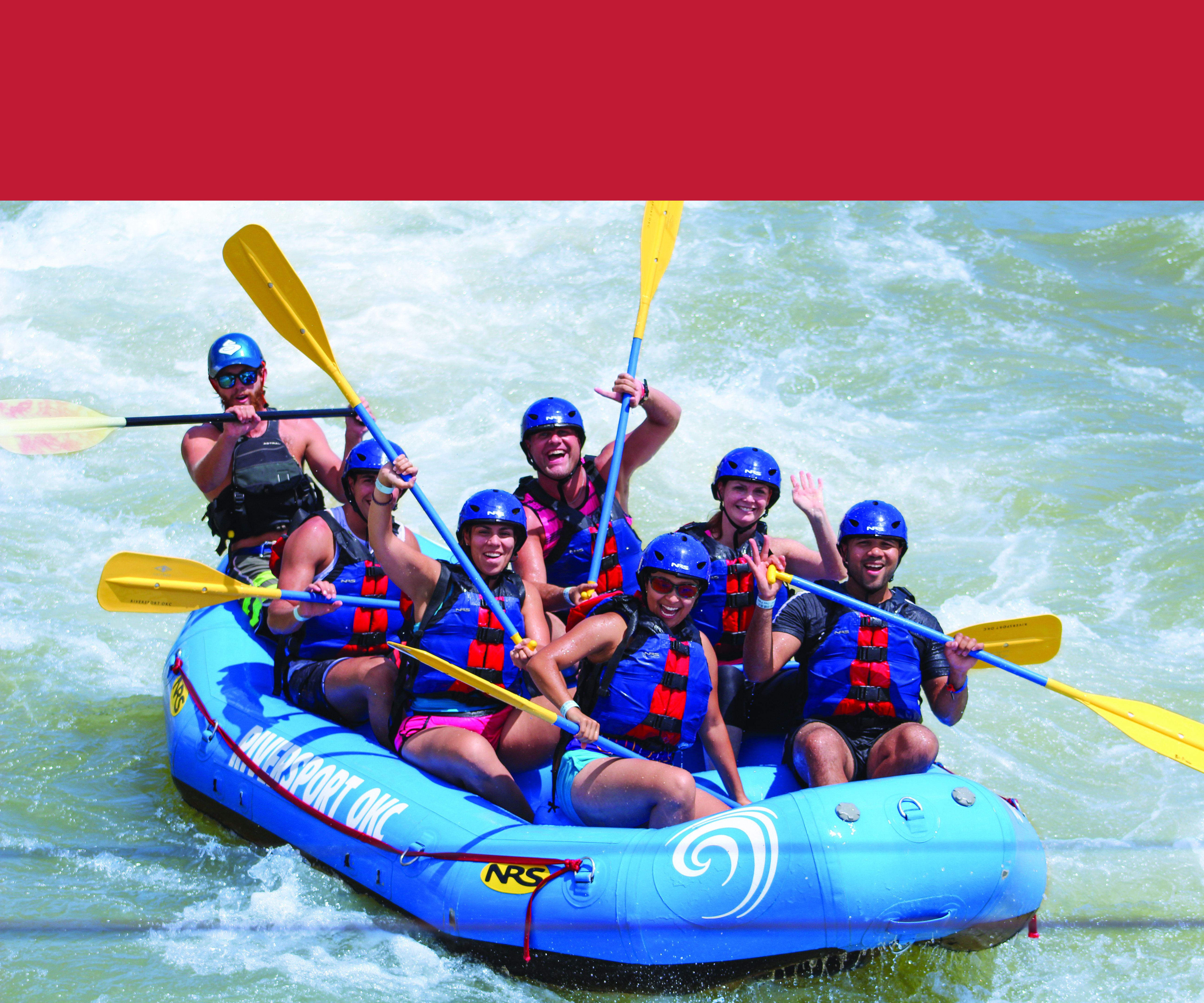 A blue raft filled with six or so people white water rafting at an outdoor facitlity. They all have helmets on for safety.