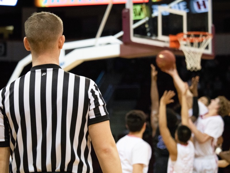 The back of a referee who is working the basketball seen in the background