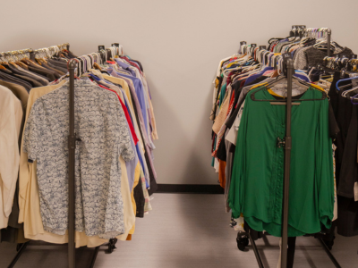 Two rolling metal garment racks filled with a variety of professional and casual clothing, organized in a brightly lit room with neutral grey walls and a white tile floor.