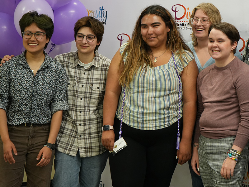 Five students smiling in front of a backdrop during Lavender Graduation