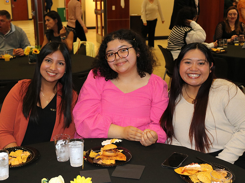 Three students smiling for the camera as they enjoy snacks at Shocker Leadership Awards