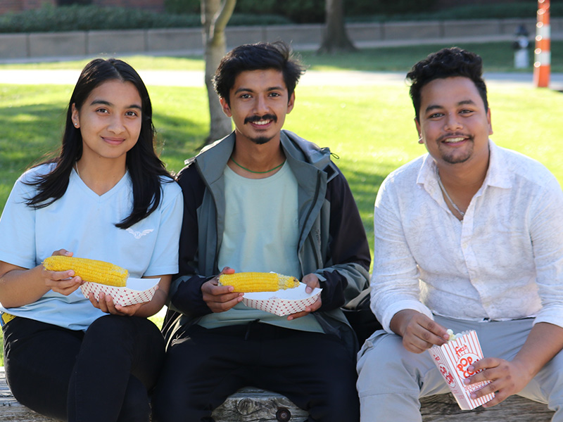 Three students at the Corn Roast eating corn and popcorn.